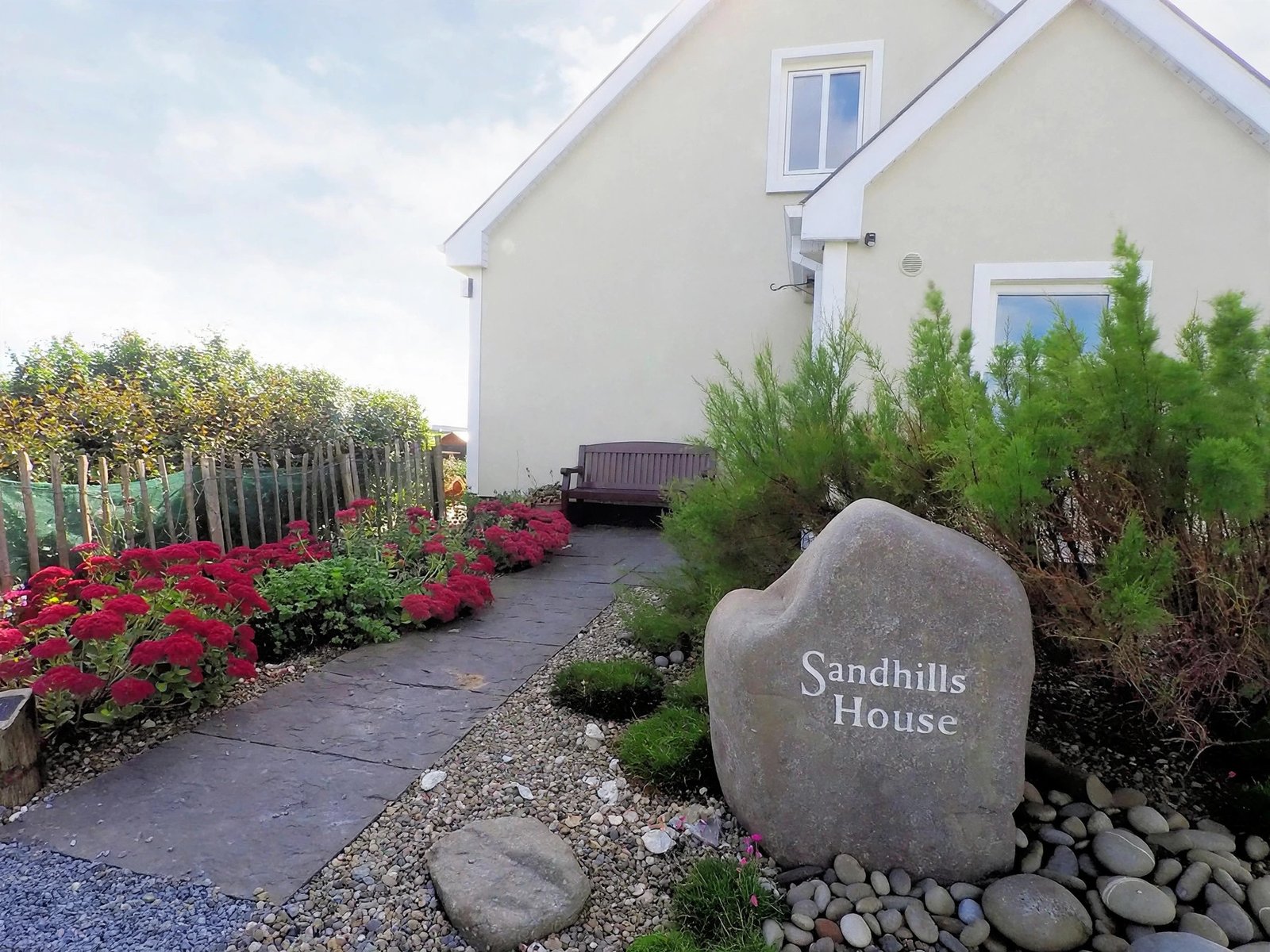 Cottage entrance with a carved stone sign, flower beds and a gravel path — enhanced sample photo