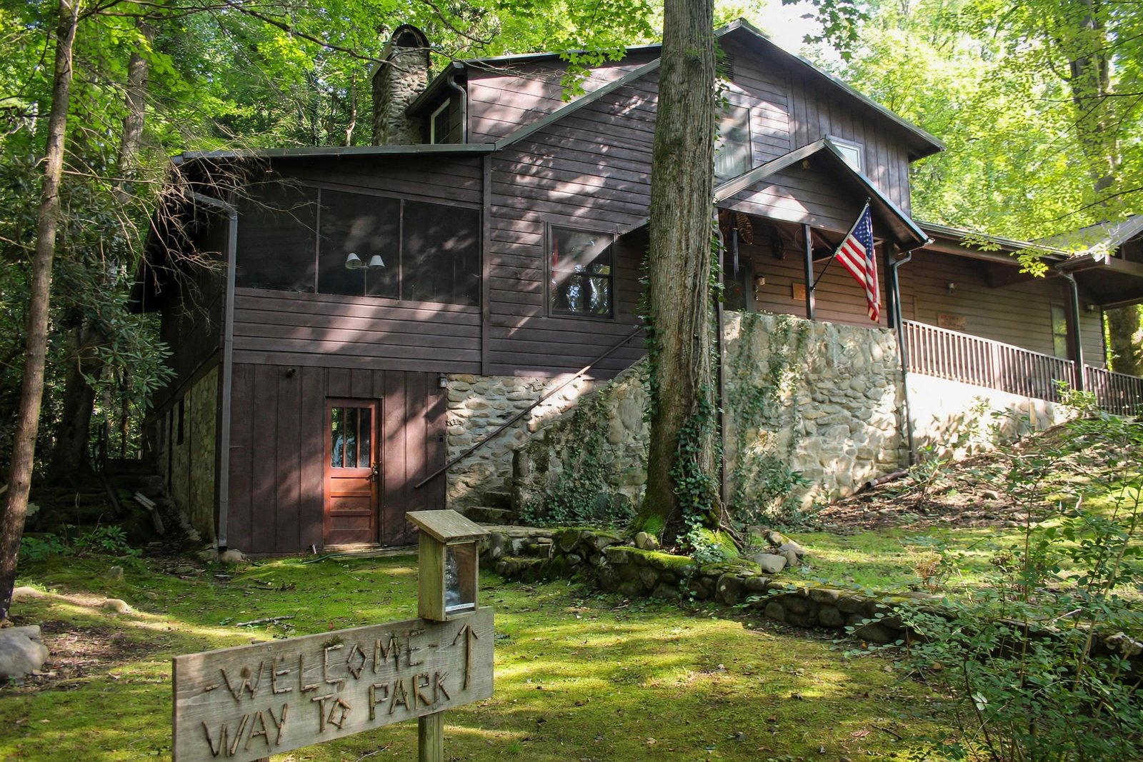 Wooden cabin among green trees with a stone patio in front — enhanced sample photo