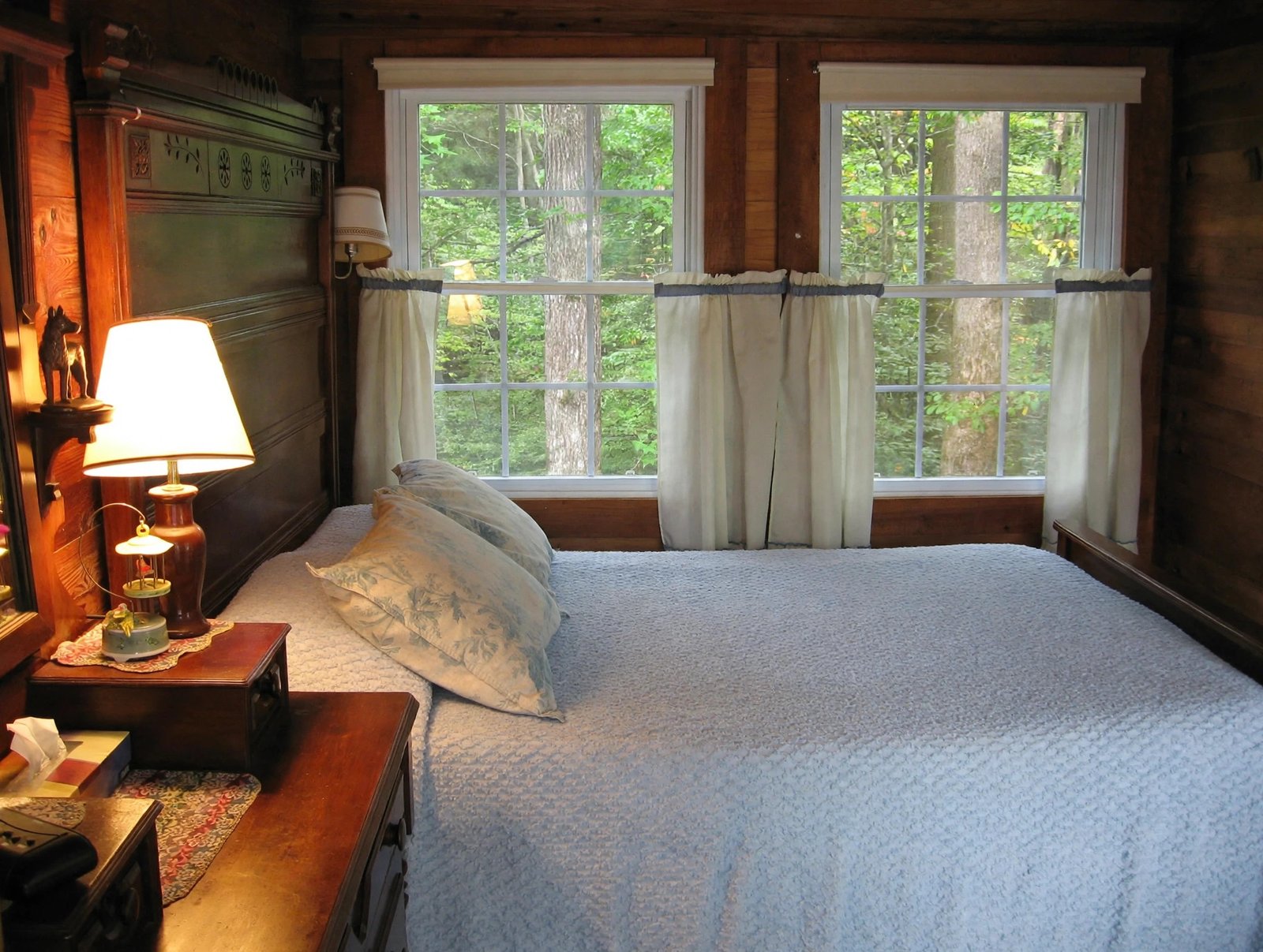 Cabin bedroom with a dressed bed, bedside lamps and woodland windows — enhanced sample photo